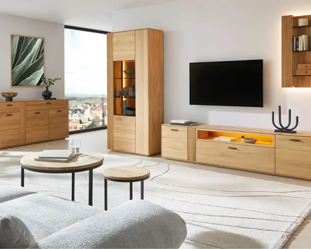 Helles Wohnzimmer mit TV-Board, Vitrine und Sideboard aus Massivholz. Moderne Wohnmöbel im natürlichen Design mit Glasfront und Beleuchtung, kombiniert mit Couchtisch und großem Teppich für stilvolles Wohnen.